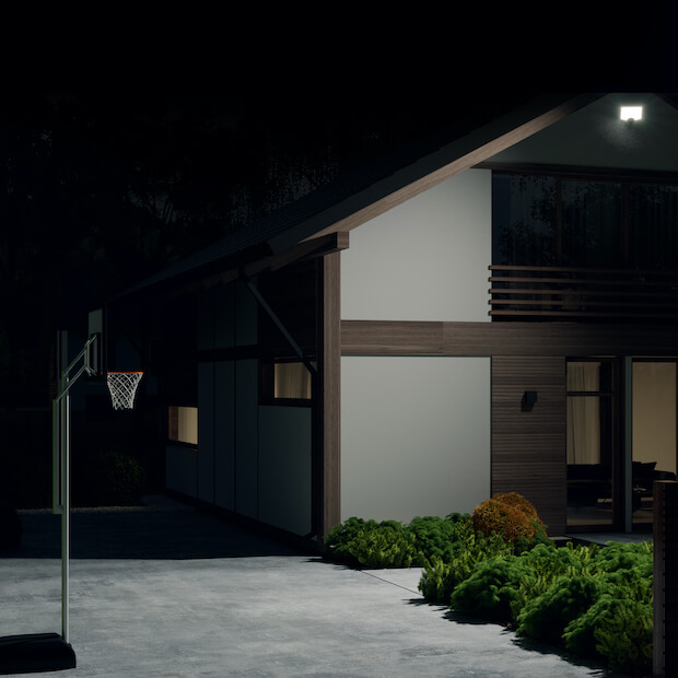 Driveway and basketball hoop at night lit with hyper bright light on a house